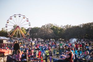 Runaway Country Music Fest, crowd sits on lawn chairs in field with ferris wheel behind